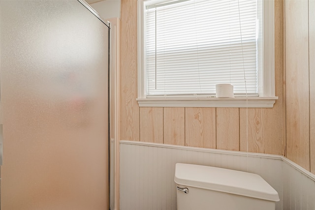 bathroom with wood walls, a shower with shower door, and toilet