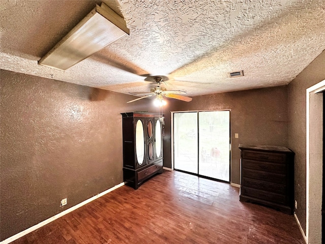 unfurnished bedroom with ceiling fan, a textured ceiling, and dark wood-type flooring