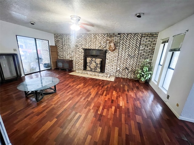 unfurnished living room featuring a textured ceiling, dark hardwood / wood-style floors, a fireplace, ceiling fan, and brick wall