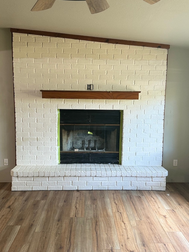 interior details with wood-type flooring, a brick fireplace, and ceiling fan