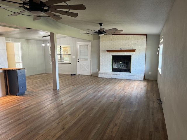 unfurnished living room with a textured ceiling, dark hardwood / wood-style floors, ceiling fan, and a brick fireplace