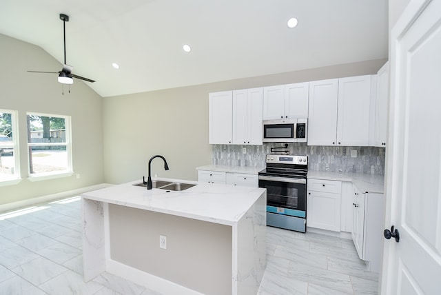 kitchen with sink, a kitchen island with sink, white cabinetry, appliances with stainless steel finishes, and vaulted ceiling