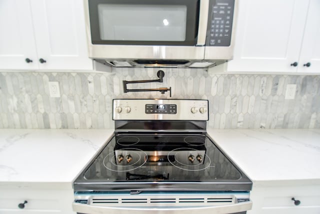 kitchen with light stone counters, white cabinets, stainless steel appliances, and backsplash