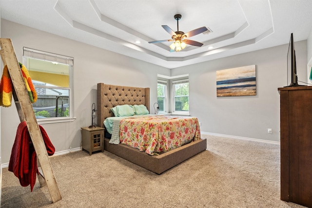 carpeted bedroom with a raised ceiling and ceiling fan