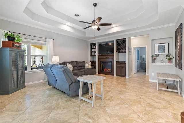 living room with a raised ceiling, ceiling fan, and crown molding