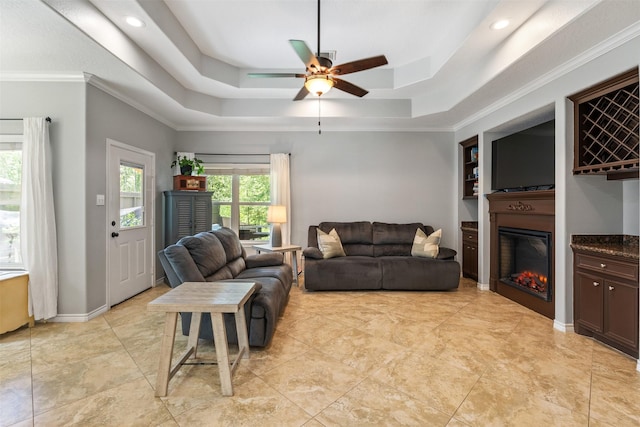 living room featuring ceiling fan, built in features, a raised ceiling, and crown molding