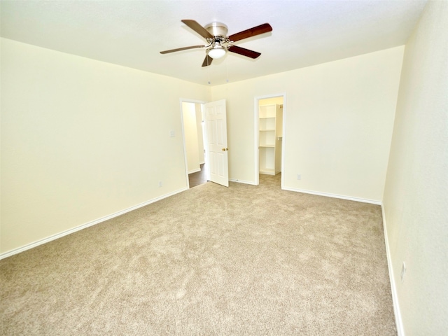 unfurnished bedroom with a closet, ceiling fan, light carpet, and a walk in closet