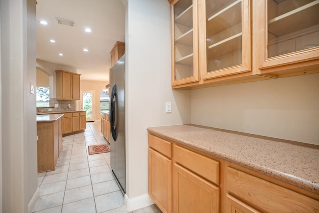 kitchen with light stone counters, light tile patterned floors, backsplash, stainless steel refrigerator, and light brown cabinetry