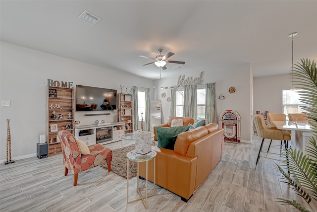 living room featuring light wood-type flooring, ceiling fan, and a fireplace