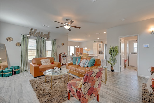 living room with light hardwood / wood-style flooring, washer / dryer, and ceiling fan with notable chandelier