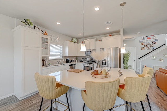 kitchen with light hardwood / wood-style floors, sink, white cabinets, stainless steel appliances, and decorative light fixtures