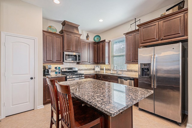 kitchen featuring light tile patterned flooring, sink, a kitchen island, appliances with stainless steel finishes, and dark stone countertops