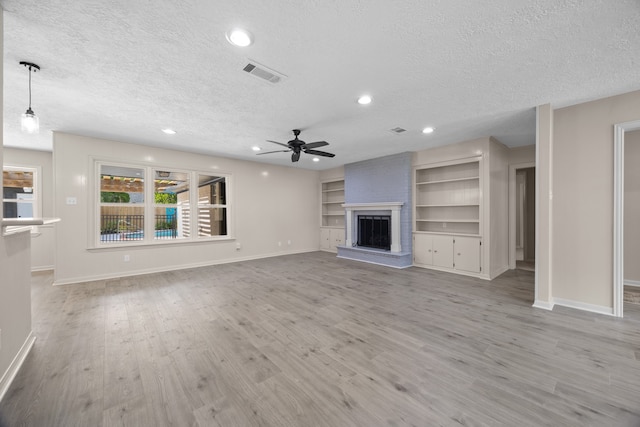 unfurnished living room featuring a brick fireplace, light hardwood / wood-style floors, ceiling fan, and a textured ceiling