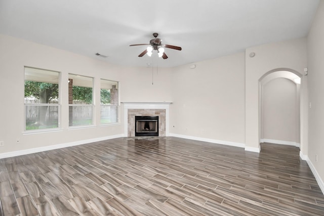 unfurnished living room featuring ceiling fan, wood-type flooring, and a tiled fireplace