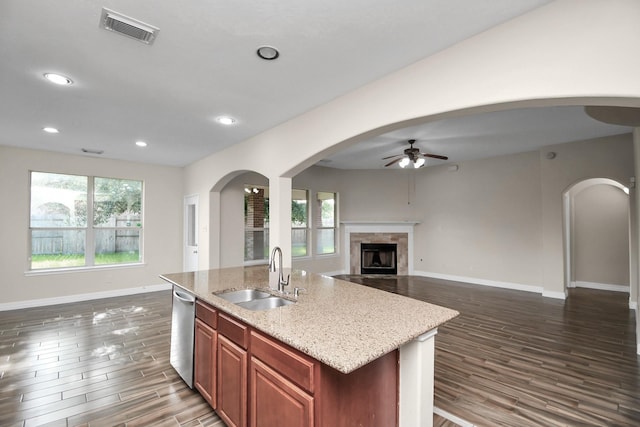 kitchen featuring a high end fireplace, stainless steel dishwasher, a kitchen island with sink, dark wood-type flooring, and sink