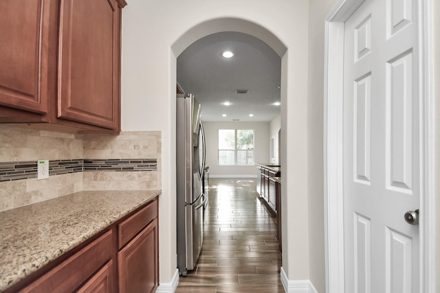 interior space with dark hardwood / wood-style flooring, light stone countertops, stainless steel fridge with ice dispenser, and decorative backsplash