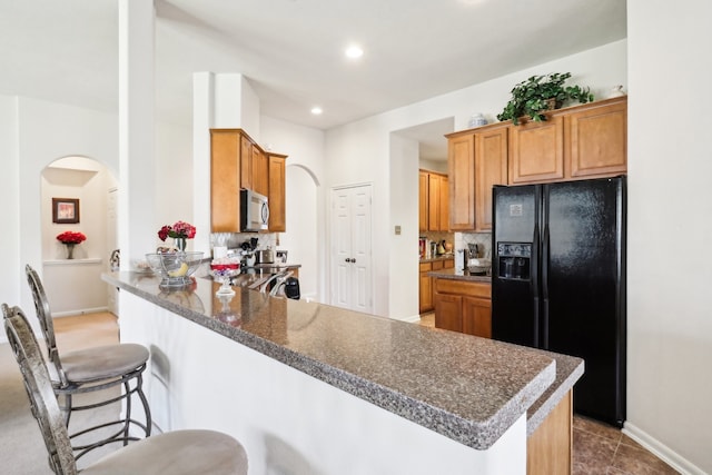 kitchen featuring decorative backsplash, kitchen peninsula, black refrigerator with ice dispenser, tile patterned flooring, and a kitchen bar