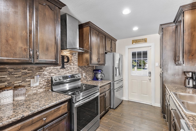 kitchen featuring appliances with stainless steel finishes, dark stone countertops, dark hardwood / wood-style flooring, sink, and wall chimney range hood