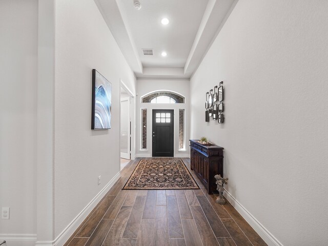 doorway to outside with a tray ceiling and dark wood-type flooring