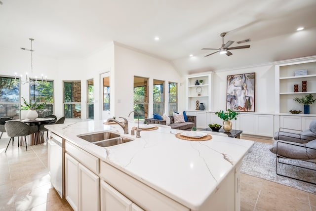 kitchen with an island with sink, light stone countertops, decorative light fixtures, and sink