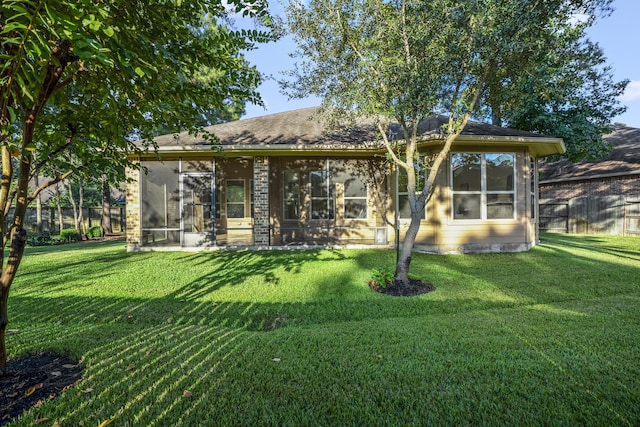 back of property with a sunroom, brick siding, a lawn, and fence