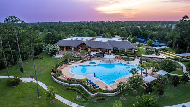 pool at dusk featuring a forest view and a community pool