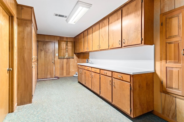 kitchen with light colored carpet, wooden walls, and sink