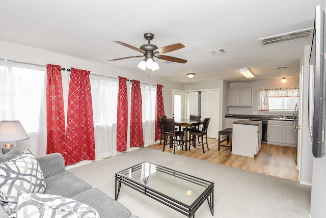 living room with a textured ceiling, ceiling fan, light hardwood / wood-style flooring, and plenty of natural light