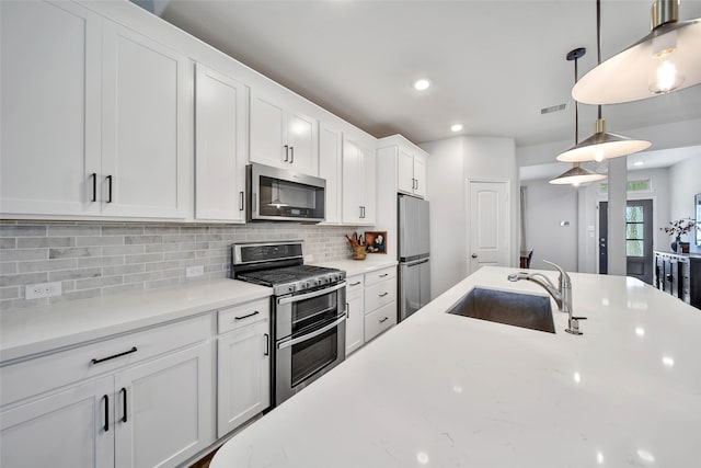 kitchen featuring pendant lighting, tasteful backsplash, sink, white cabinets, and stainless steel appliances