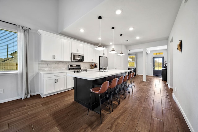 kitchen with white cabinets, an island with sink, pendant lighting, appliances with stainless steel finishes, and dark hardwood / wood-style floors