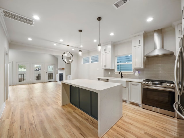 kitchen with wall chimney exhaust hood, stainless steel appliances, white cabinetry, and a center island