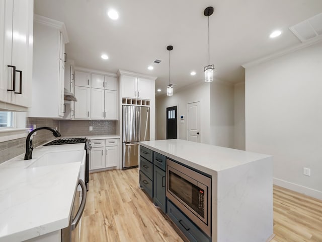 kitchen with light hardwood / wood-style floors, white cabinetry, built in appliances, a center island, and decorative light fixtures