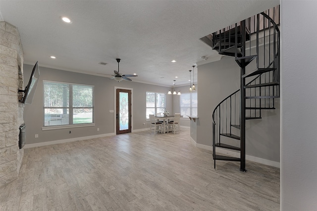 unfurnished living room with ceiling fan with notable chandelier, light wood-type flooring, and a textured ceiling