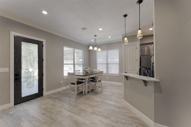 dining area featuring light hardwood / wood-style flooring, a textured ceiling, an inviting chandelier, and crown molding