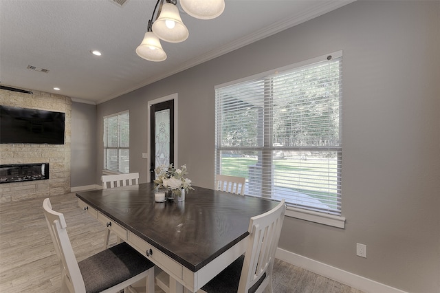 dining area featuring light wood-type flooring, a healthy amount of sunlight, a stone fireplace, and ornamental molding