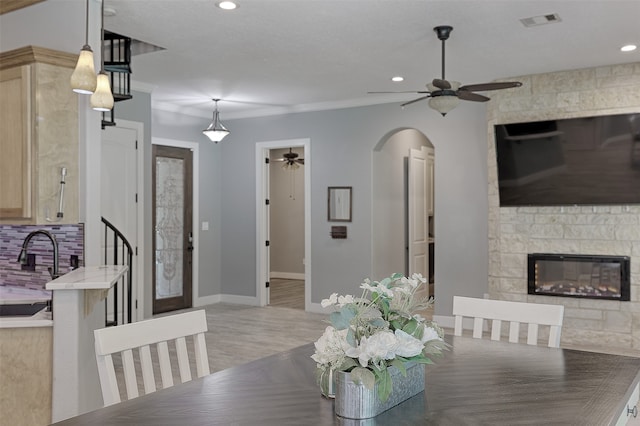 dining room featuring light wood-type flooring, ceiling fan, a fireplace, and sink