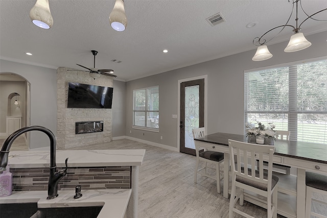 interior space featuring light stone counters, sink, a stone fireplace, decorative light fixtures, and light hardwood / wood-style flooring