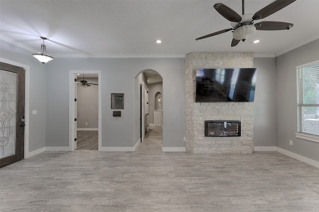 unfurnished living room with a stone fireplace, a textured ceiling, light hardwood / wood-style floors, and crown molding