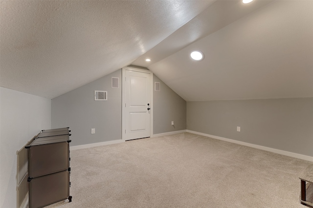 additional living space with a textured ceiling, vaulted ceiling, and light carpet