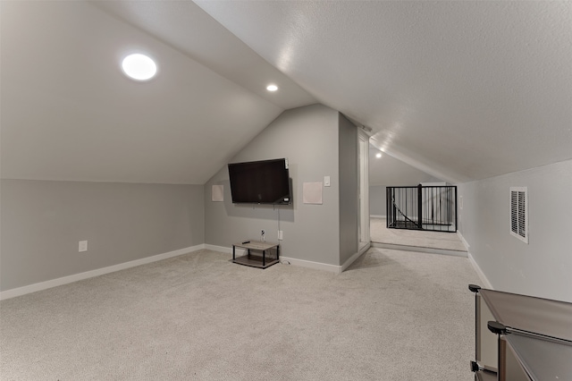 additional living space featuring light carpet, vaulted ceiling, and a textured ceiling