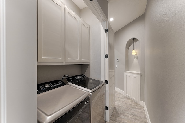 washroom with light wood-type flooring, washer and dryer, and cabinets