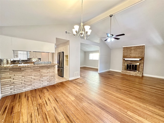 unfurnished living room with light hardwood / wood-style floors, high vaulted ceiling, ceiling fan with notable chandelier, a fireplace, and beam ceiling