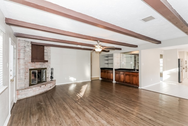 unfurnished living room featuring wood-type flooring, a brick fireplace, and beam ceiling