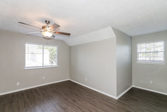 unfurnished room featuring a textured ceiling, a healthy amount of sunlight, vaulted ceiling, and dark wood-type flooring