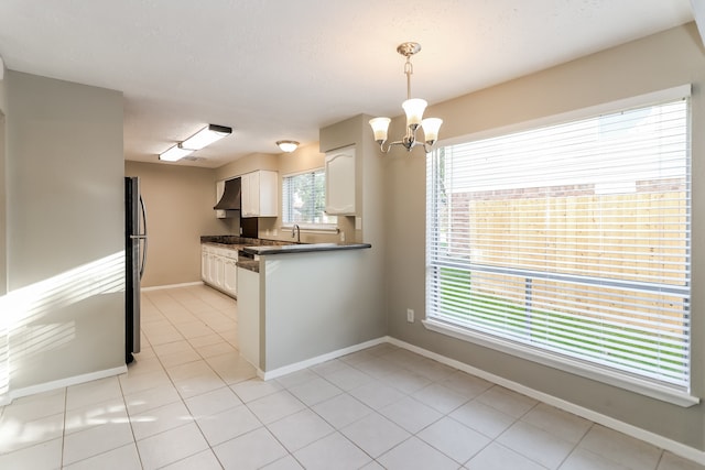 kitchen featuring premium range hood, white cabinetry, hanging light fixtures, an inviting chandelier, and stainless steel fridge