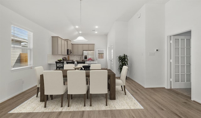 dining area with high vaulted ceiling and light hardwood / wood-style flooring