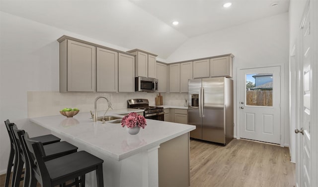 kitchen featuring lofted ceiling, sink, appliances with stainless steel finishes, a kitchen bar, and kitchen peninsula