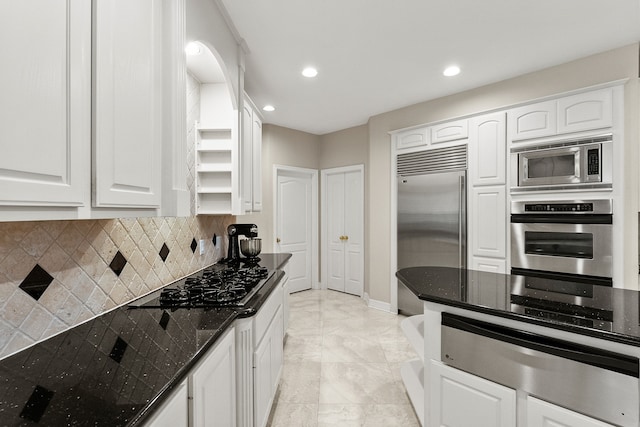 kitchen featuring dark stone counters, decorative backsplash, white cabinetry, and built in appliances