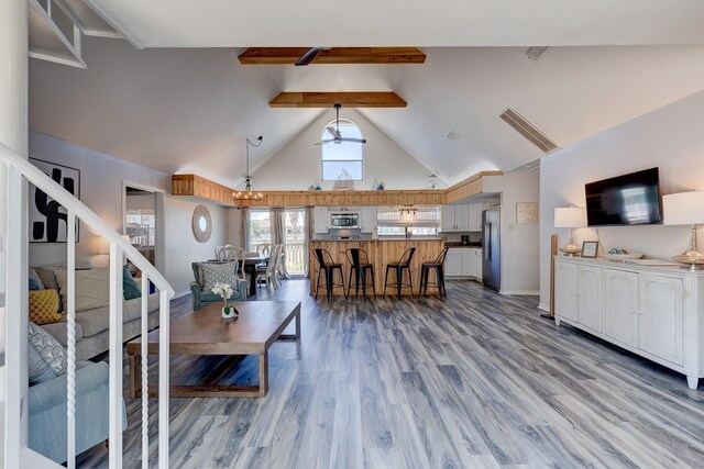 living room featuring beam ceiling, stairway, light wood-style floors, high vaulted ceiling, and baseboards