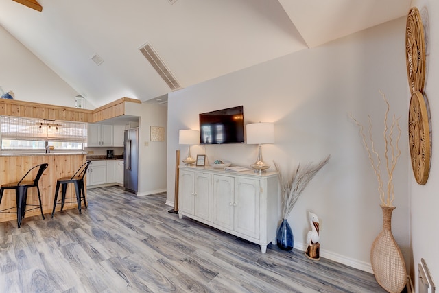 kitchen with white cabinetry, a breakfast bar, high quality fridge, high vaulted ceiling, and light wood-type flooring